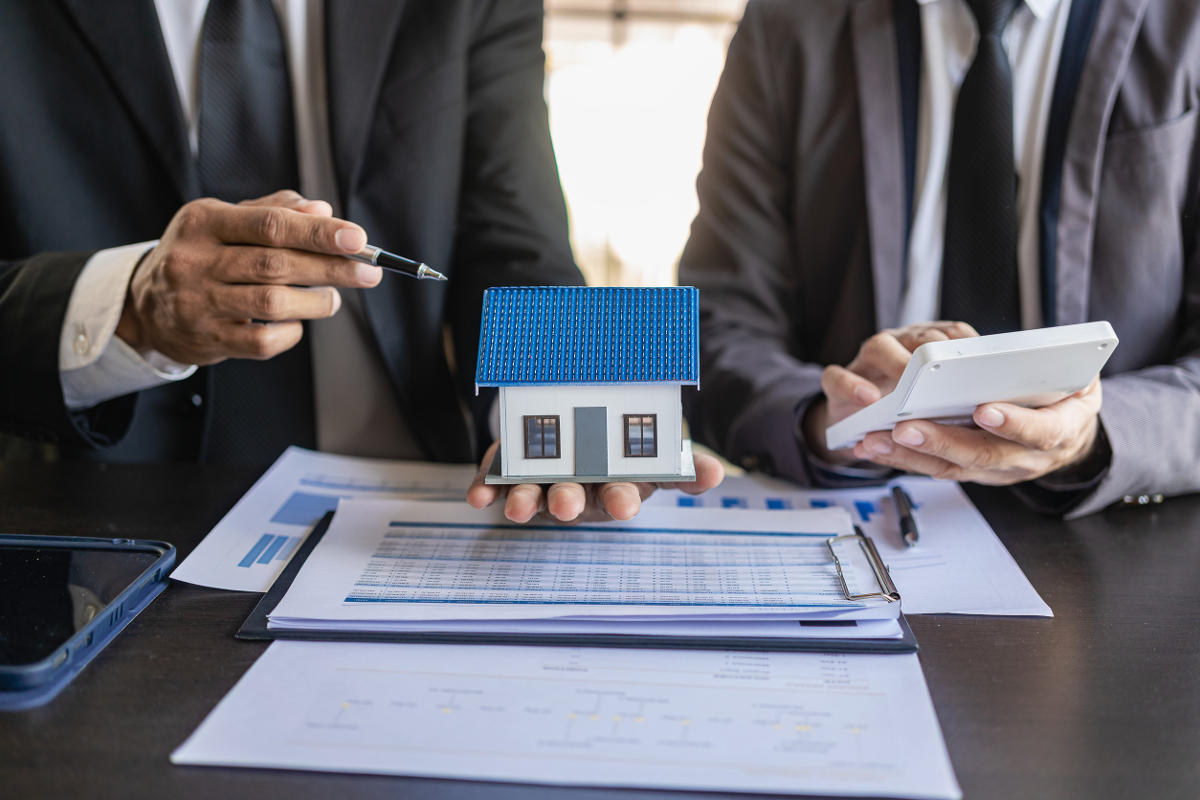 Two men looking at a model house holding a pen and a calculator