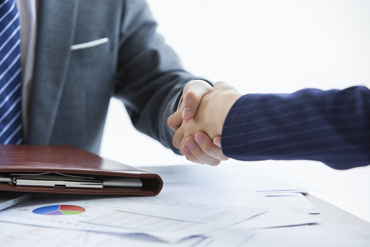 Two men shaking hands over a contract and paperwork